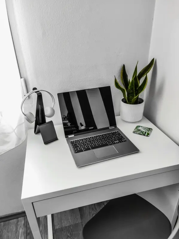 Góc bàn làm việc gọn gàng có laptop, tai nghe, điện thoại và một chậu cây cảnh nhỏ