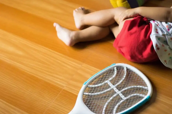 Vợt điện diệt côn trùng đặt trên nền nhà gỗ bên cạnh đôi chân của một đứa trẻ